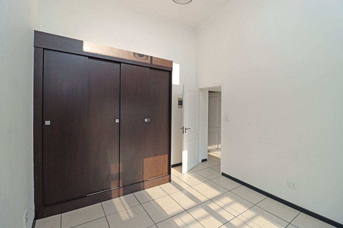 A bright, empty bedroom featuring neutral tiled flooring and a large, dark wood built-in wardrobe.