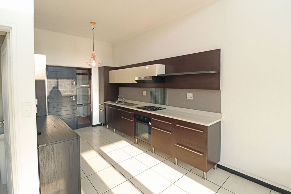 Modern kitchen featuring dark wood cabinetry, stone countertops, built-in oven, gas hob, and tiled flooring in a clean, open-plan layout.
