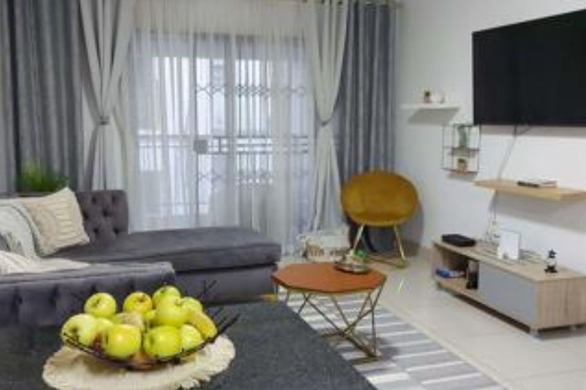 A well-maintained living room featuring tiled flooring, floating wall shelves, and a large sliding glass door with an integrated security gate.