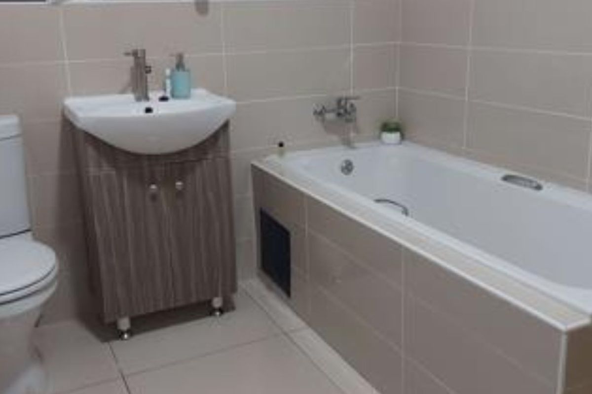 A modern bathroom featuring a tiled bathtub, vanity cabinet with basin, and neutral wall tiling.