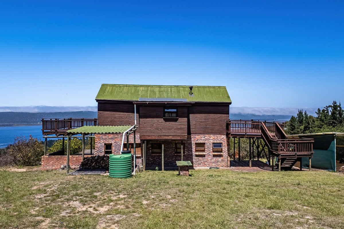 Rear view of a two-story farm house featuring timber cladding, brick base, raised wooden decks, and a scenic landscape view.