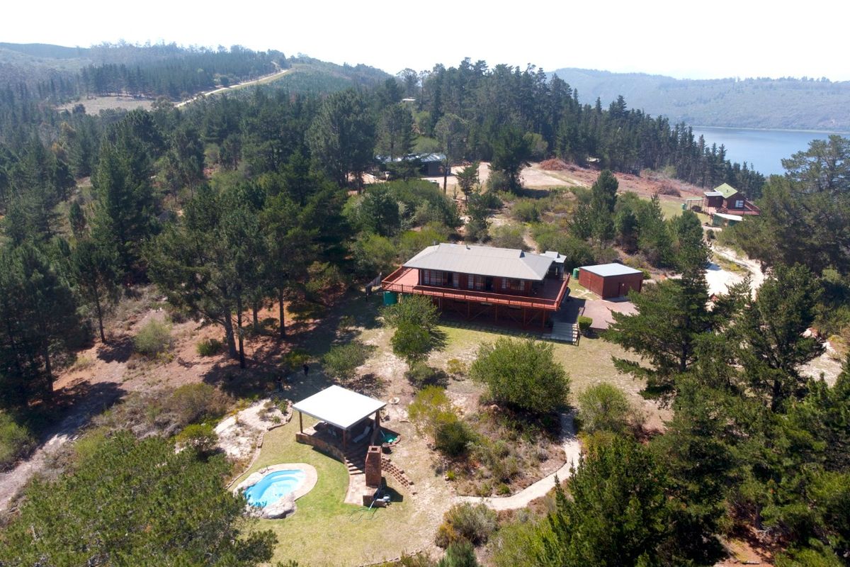 Aerial view of a rural property featuring a main dwelling with a large timber deck, a swimming pool, and a separate outdoor entertainment area.