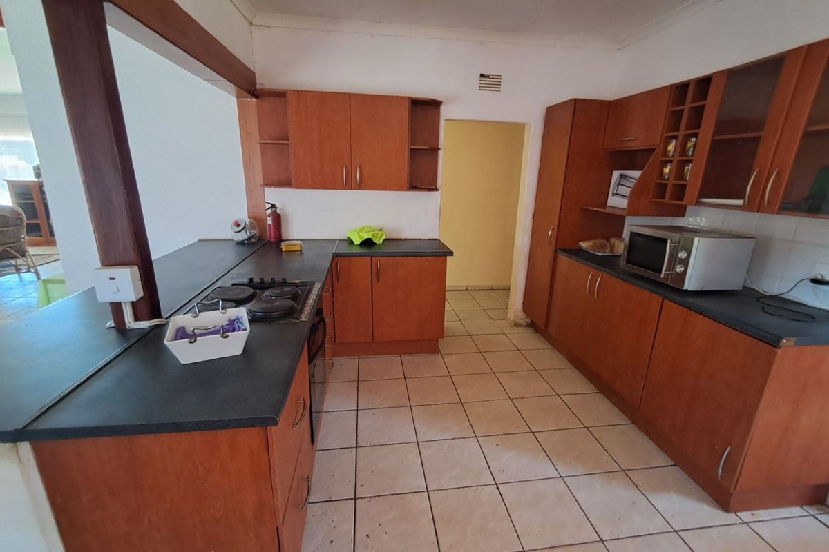 A dated kitchen featuring wooden cabinetry, dark laminate countertops, a gas hob, and tiled flooring, offering potential for a modern renovation.