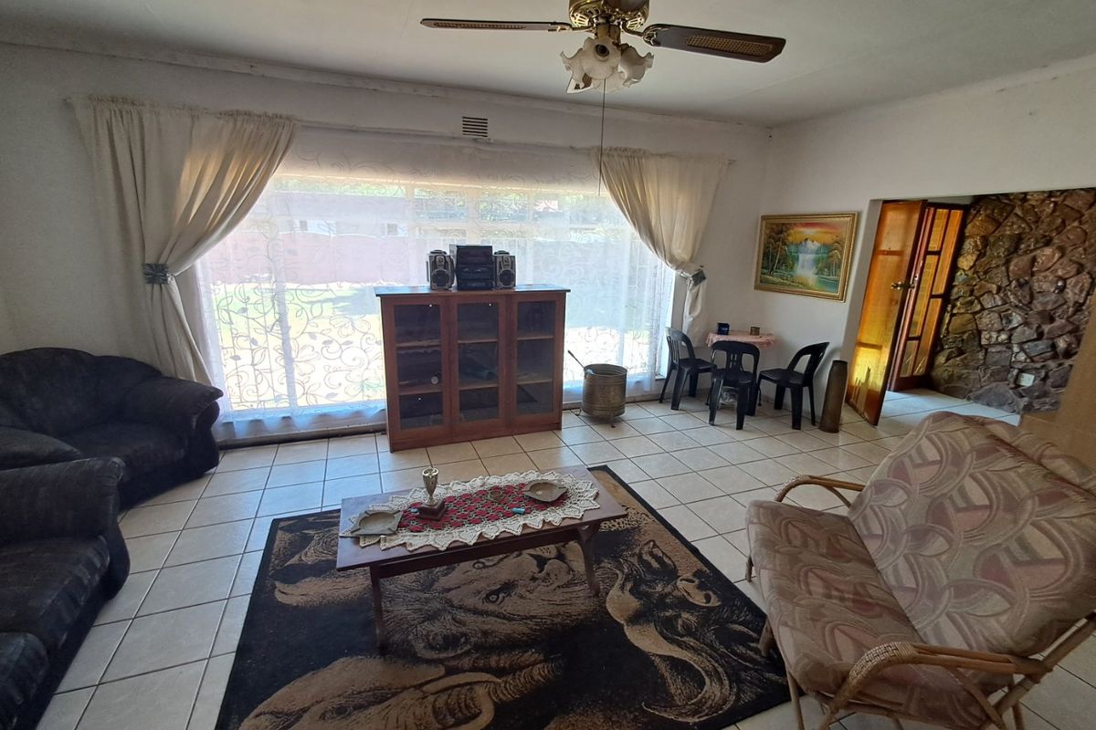 Spacious living room featuring tiled flooring, a ceiling fan, and a rustic stone feature wall, offering a dated but functional layout.