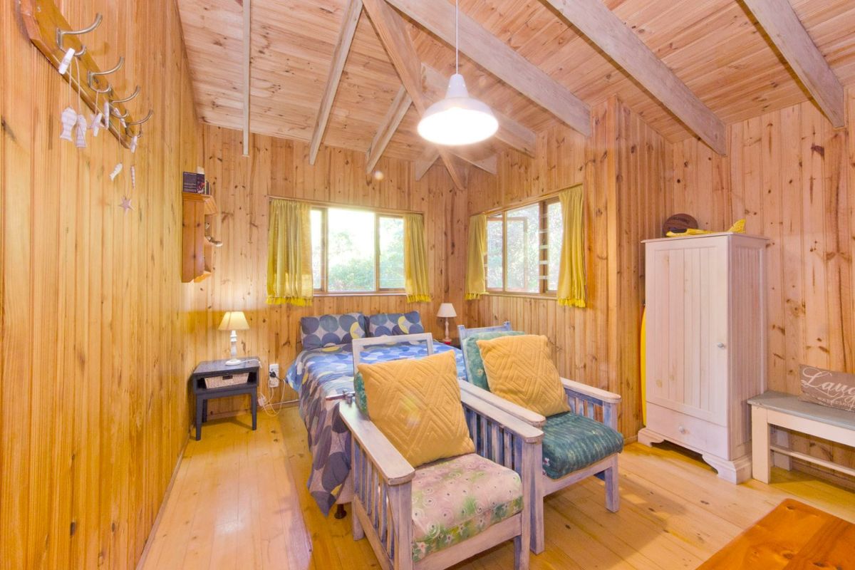 A cozy bedroom featuring warm timber wall cladding, exposed rafters, and timber flooring, creating a rustic and inviting atmosphere.