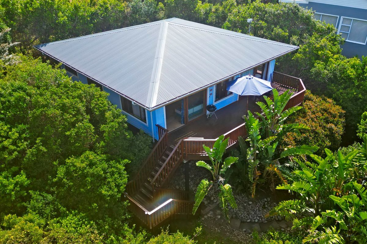 Aerial view of a detached house featuring a metal roof, a spacious elevated timber deck, and a wooden staircase set within a lush garden.