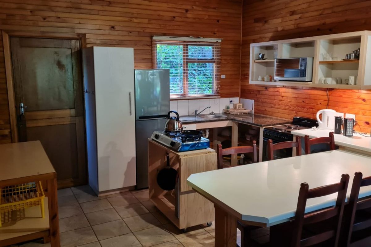 A rustic kitchen featuring timber wall cladding, tiled flooring, built-in cabinetry, and functional cooking appliances in a compact layout.