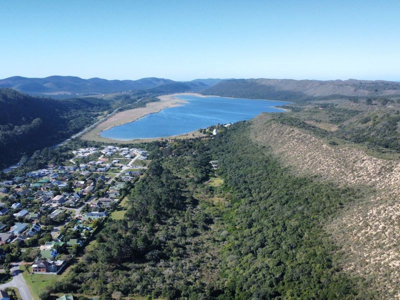 An aerial view of the coastal residential area, showcasing the surrounding natural landscape, hills, and proximity to the lagoon.