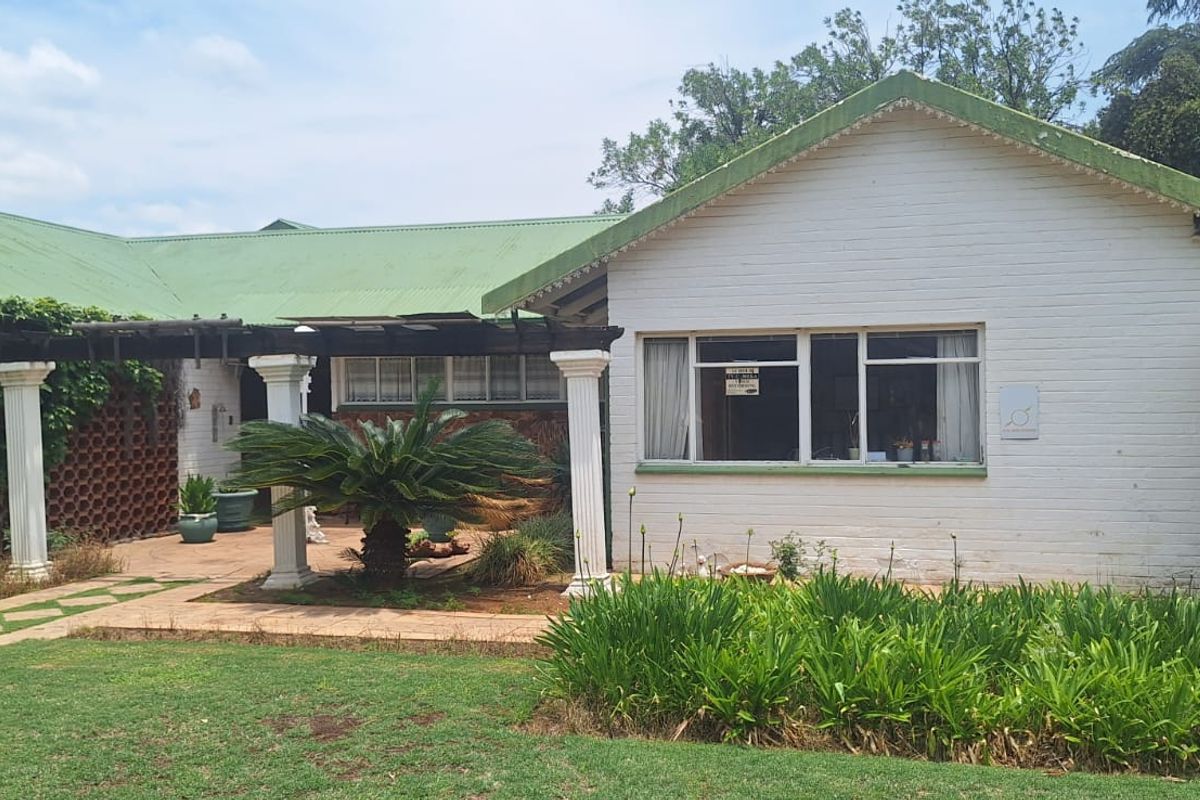 Rear exterior view of the house featuring a paved patio area, pergola, and established garden landscaping.