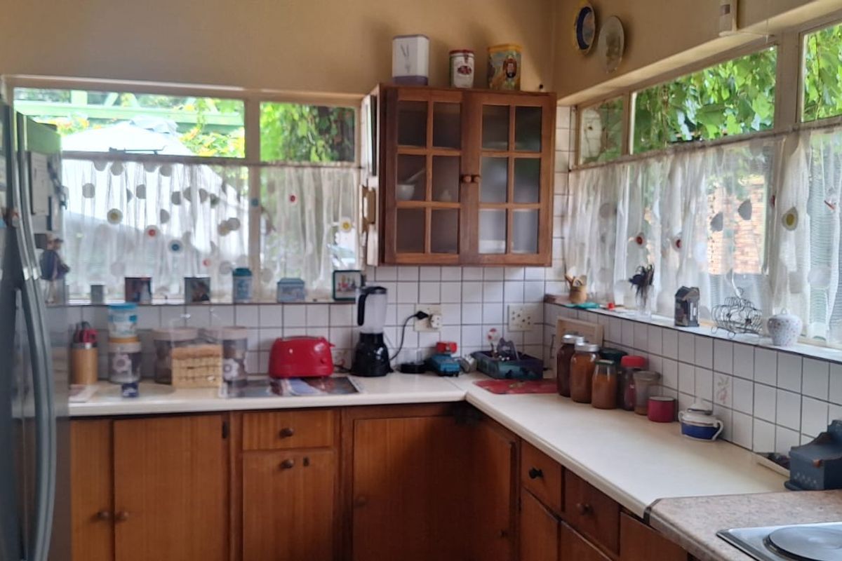 A functional kitchen featuring wooden cabinetry, tiled backsplash, and ample natural light from large windows overlooking the garden.