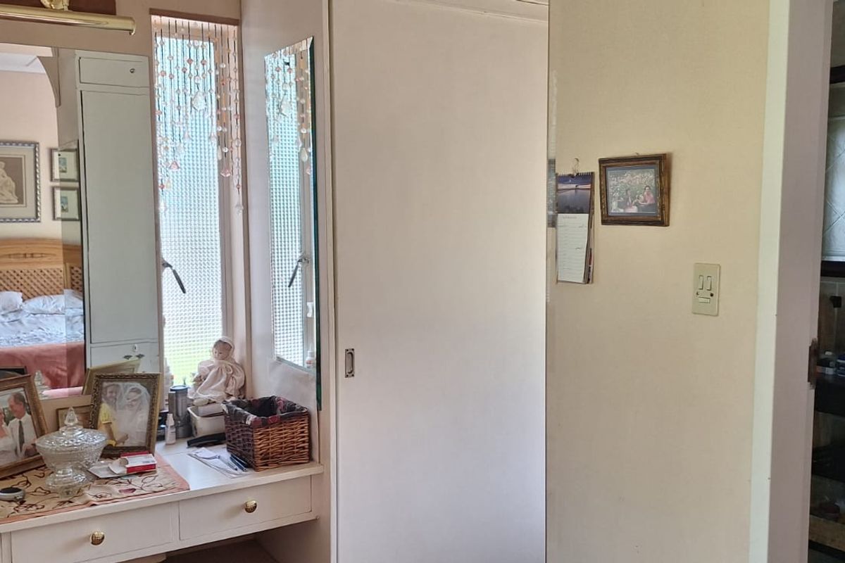 Bedroom featuring a built-in vanity area with integrated mirrors and lighting, adjacent to a bathroom with a tiled vanity unit.