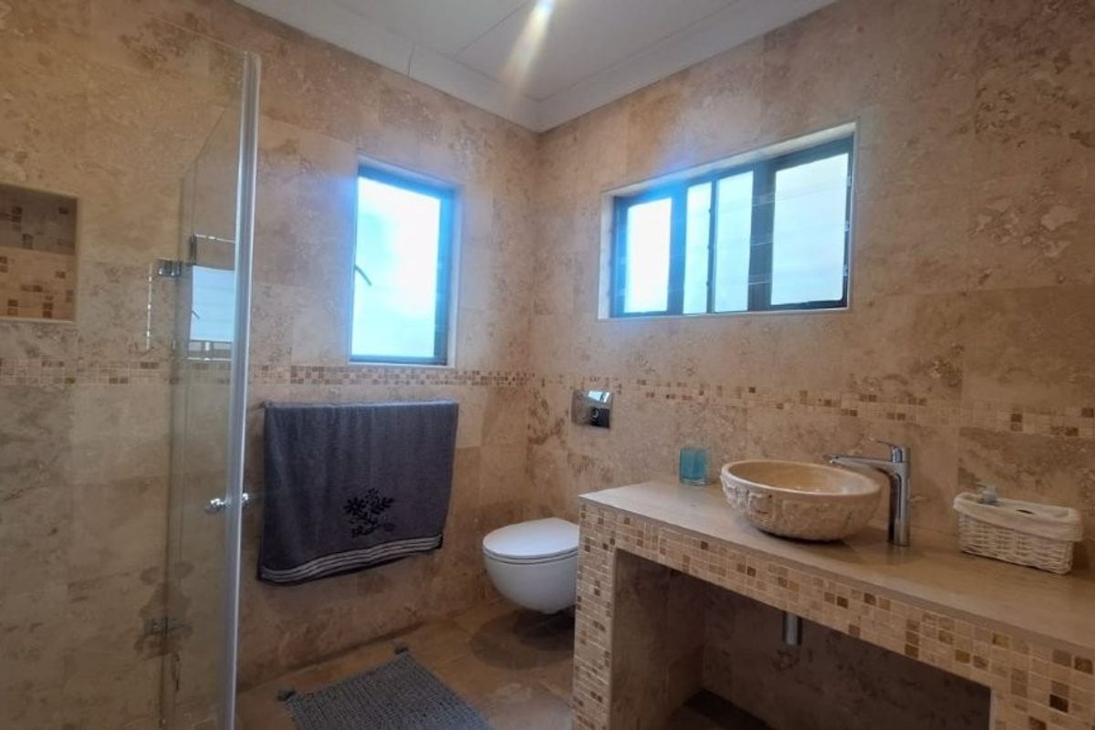 A modern bathroom featuring floor-to-ceiling travertine tiling, a stone vessel sink on a tiled vanity, and a glass-enclosed shower with a built-in niche.