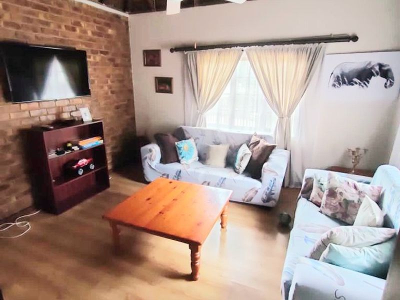 A cozy living room featuring a rustic thatched ceiling, exposed brick wall, and laminate flooring, creating a warm and inviting atmosphere.