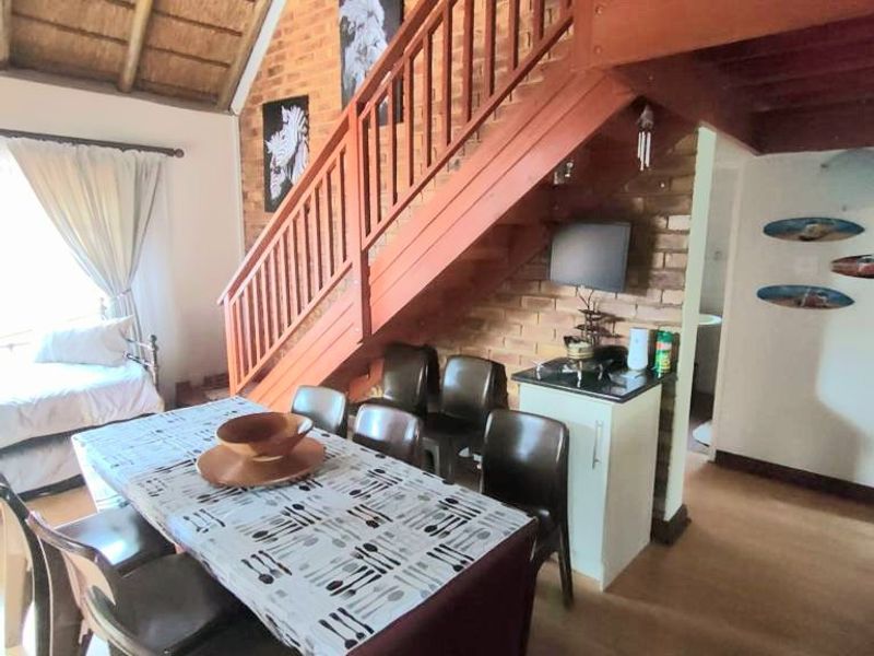 Open plan living area featuring a distinctive thatched roof, exposed brick walls, and a timber staircase leading to an upper level.