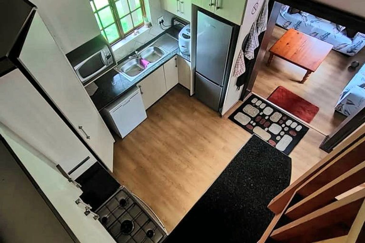 A compact kitchen featuring built-in cabinetry, a gas hob, and a double sink, set under a traditional thatched roof with laminate flooring.