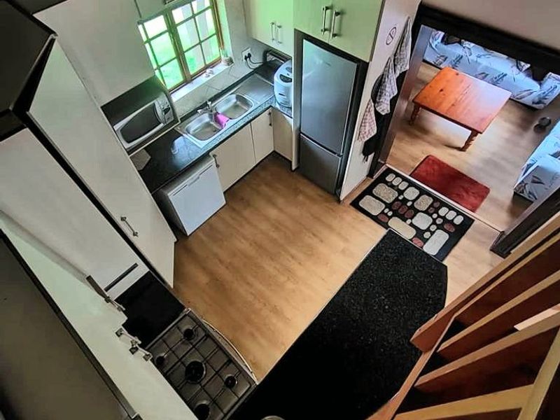 A compact kitchen featuring built-in cabinetry, a gas hob, and a double sink, set under a traditional thatched roof with laminate flooring.
