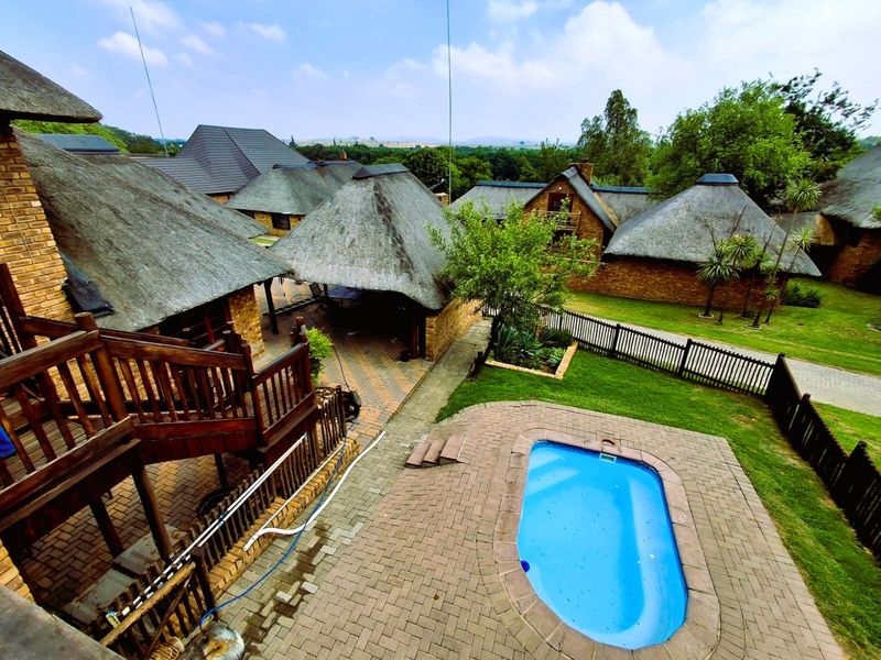 Elevated view of a residential property featuring a swimming pool, brick paved patio, and multiple buildings with traditional thatched roofs set in a garden.