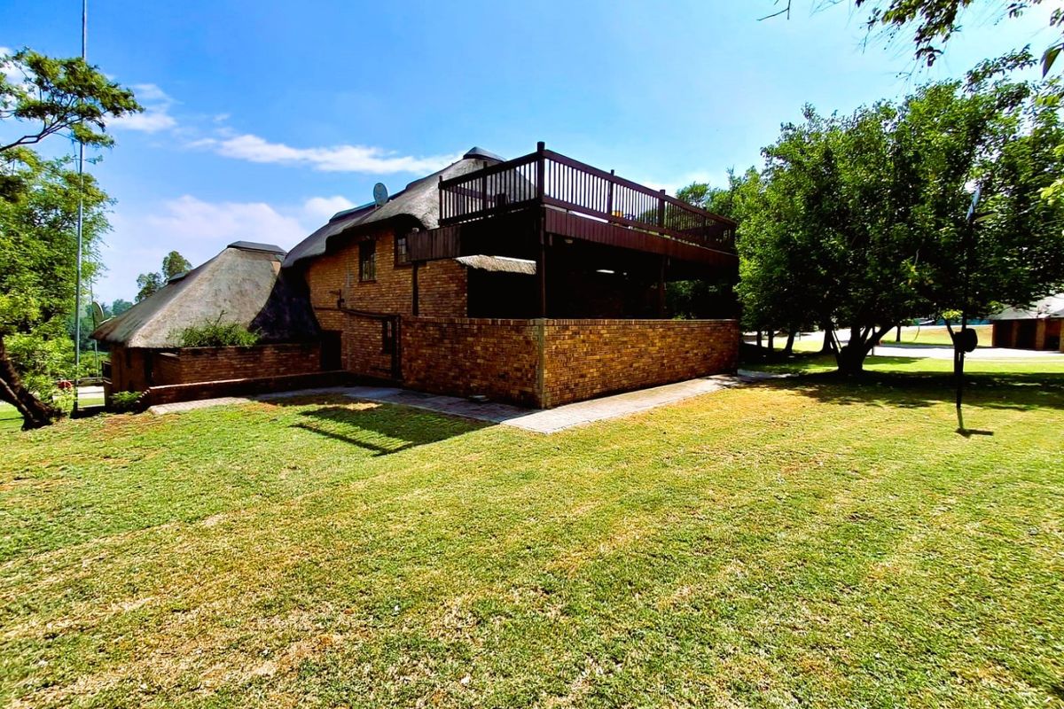 Rear view of a brick house featuring a thatched roof and a raised wooden deck overlooking a spacious garden.