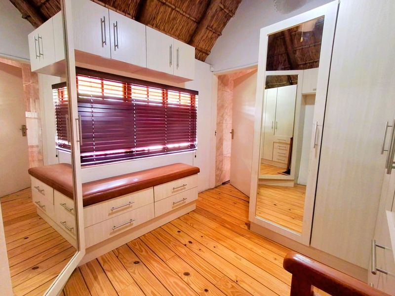 A well-maintained bedroom featuring timber flooring, a unique thatch ceiling, and extensive built-in cabinetry with integrated mirrored wardrobe doors.