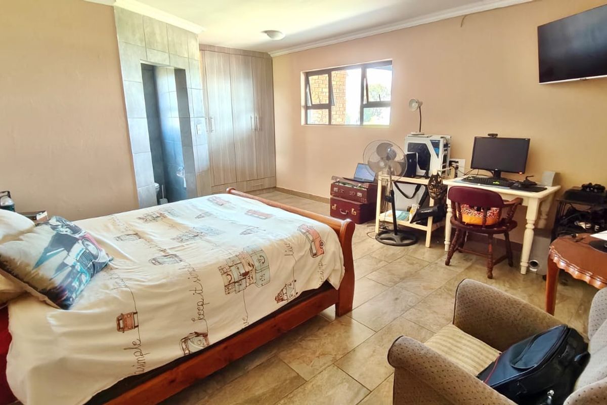 Spacious bedroom featuring tiled flooring, built-in cupboards, and an en-suite bathroom entrance, offering a functional layout with natural light.