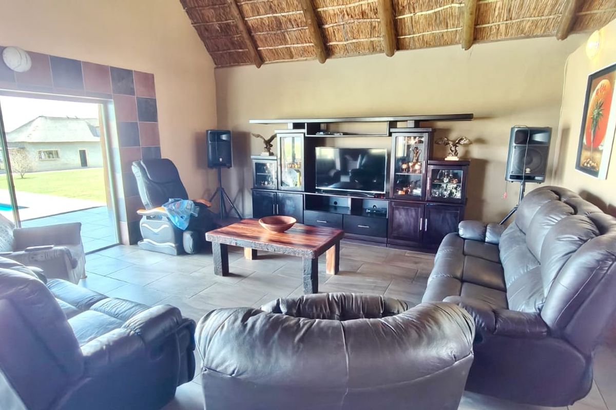 Spacious living room featuring a high thatched ceiling with exposed timber rafters, tiled flooring, and large sliding glass doors leading to the outdoor area.