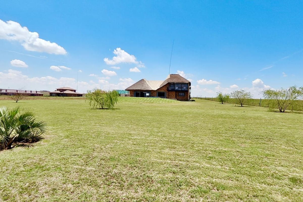 A wide-angle view of the rear elevation of a large thatched-roof house set within a spacious, well-maintained grassy landscape.