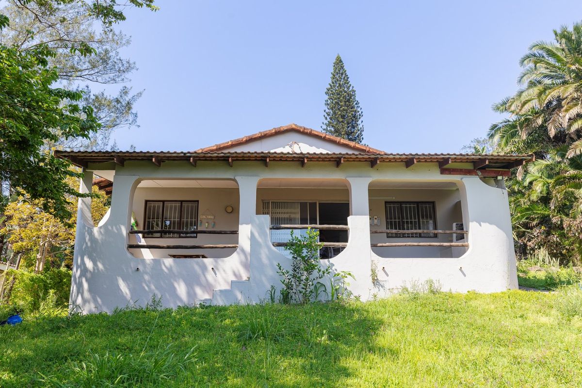 Rear view of a single-story house featuring a covered patio, terracotta roof tiles, and security bars on windows, set within a garden area.