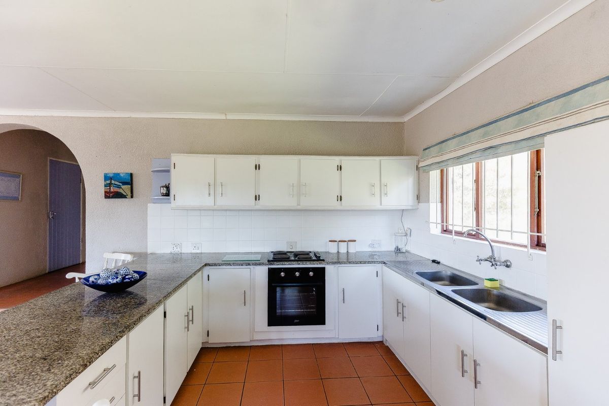 Functional kitchen featuring granite countertops, built-in oven, gas hob, double stainless steel sink, and ample cabinetry with terracotta floor tiles.