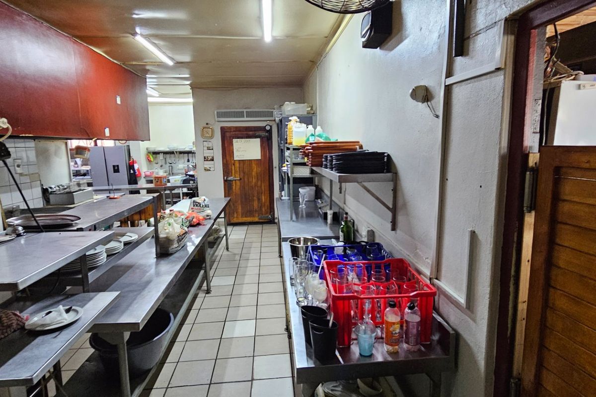 A commercial kitchen prep area featuring stainless steel work surfaces, tiled flooring, and functional storage shelving for food service operations.