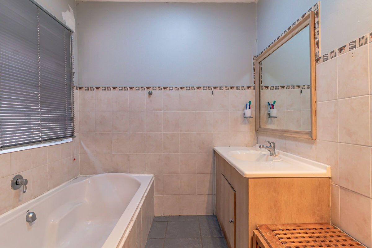 A functional bathroom featuring a built-in bathtub, vanity cabinet with integrated sink, and neutral wall tiling. The space is ready for a modern update.