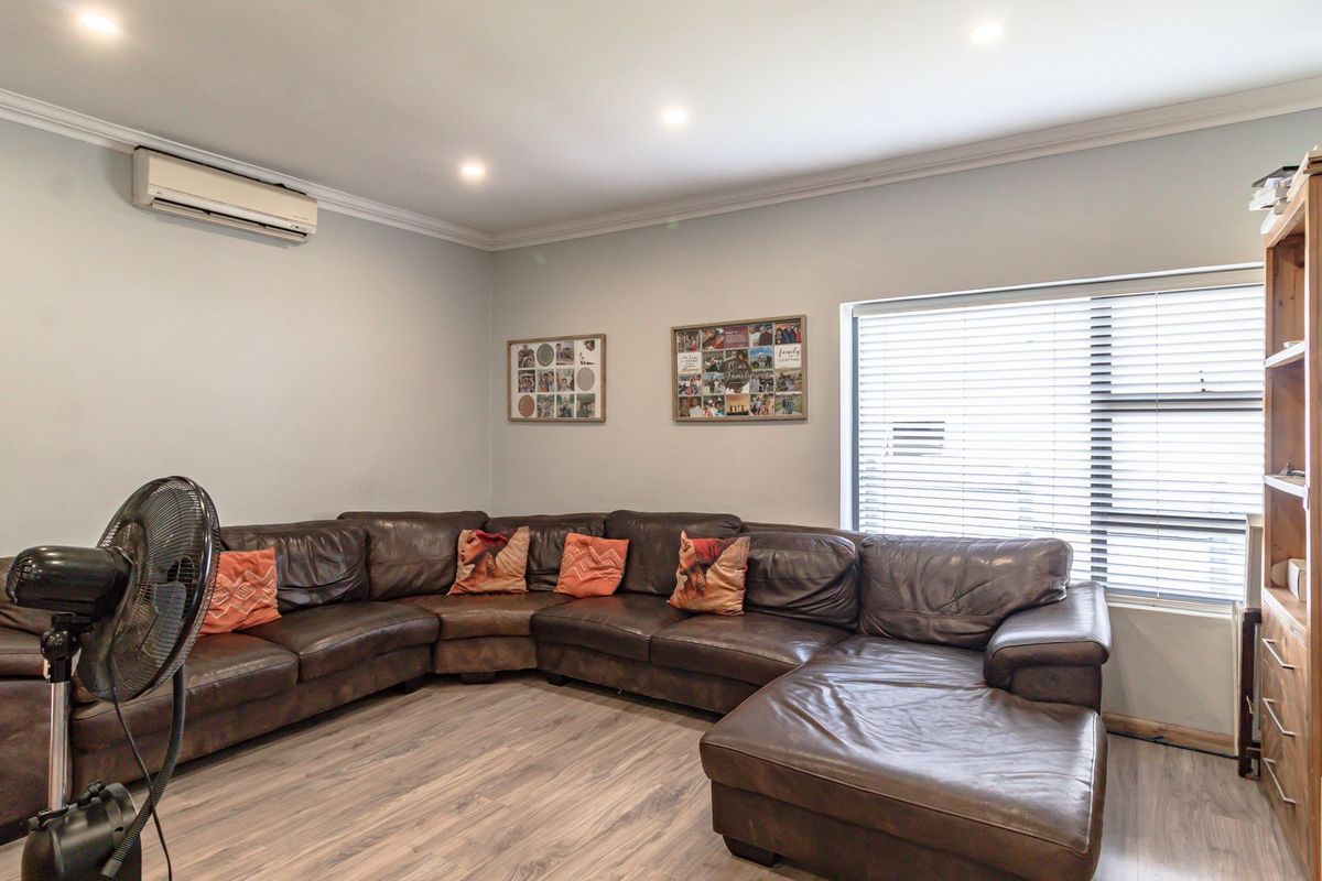 A comfortable living room featuring laminate flooring, recessed downlighting, and a wall-mounted split-system air conditioner for climate control.