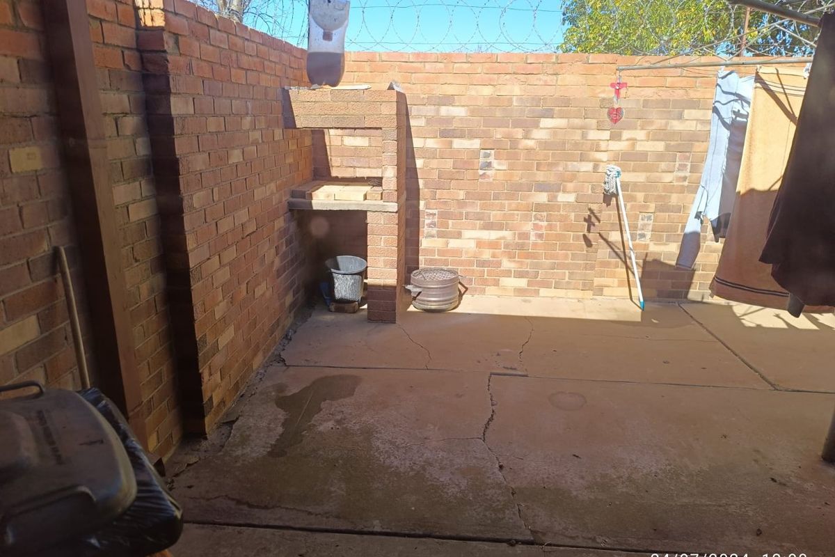 A private rear courtyard featuring a built-in brick braai, concrete paving, and secure boundary walls topped with razor wire.