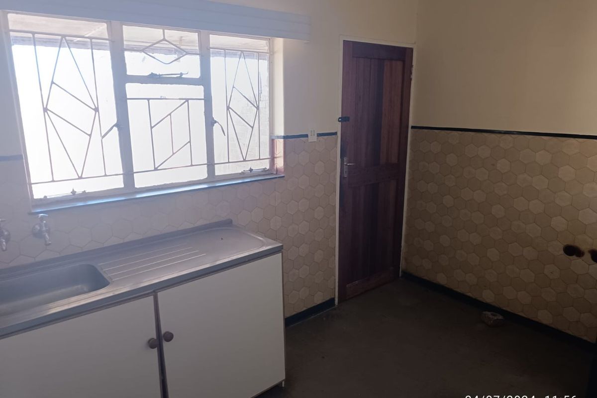 A functional kitchen area featuring a stainless steel sink, built-in cabinetry, and tiled splashbacks, currently in a vacant and dated condition.