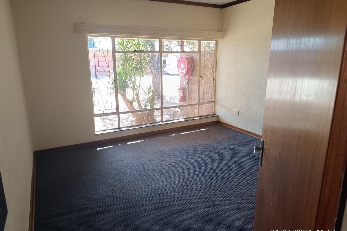 An empty bedroom featuring carpeted flooring and a large window with security bars, offering a view of the exterior area.