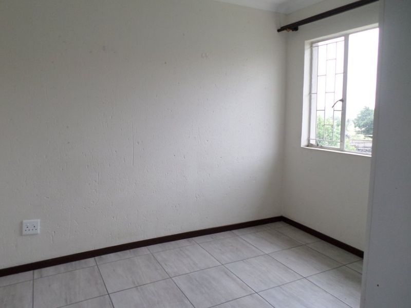 An empty bedroom featuring neutral tiled flooring, a window with security bars, and plain white walls ready for personalization.