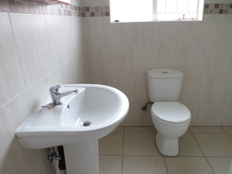 A functional bathroom featuring a pedestal basin, chrome mixer tap, ceramic toilet, and neutral wall and floor tiling.