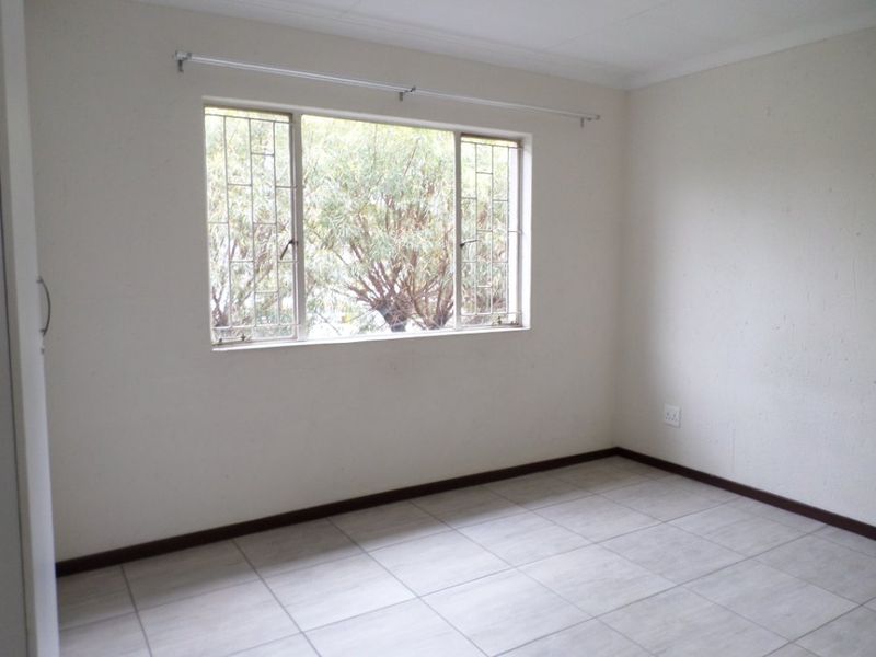 A bright, empty bedroom featuring neutral tiled flooring, a window with security bars, and a curtain rail, ready for personalization.