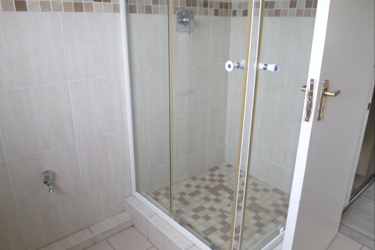 A functional bathroom featuring a glass-enclosed shower with tiled walls, mosaic accents, and neutral floor tiling.