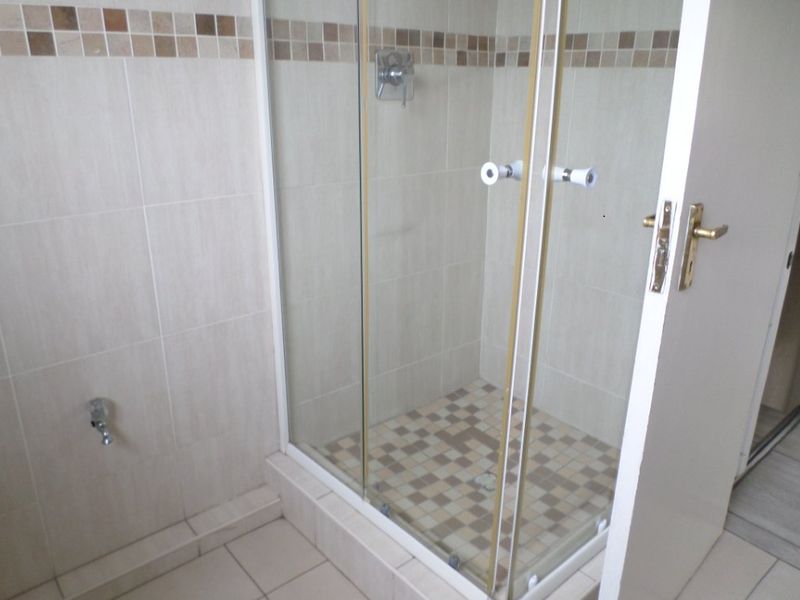 A functional bathroom featuring a glass-enclosed shower with tiled walls, mosaic accents, and neutral floor tiling.