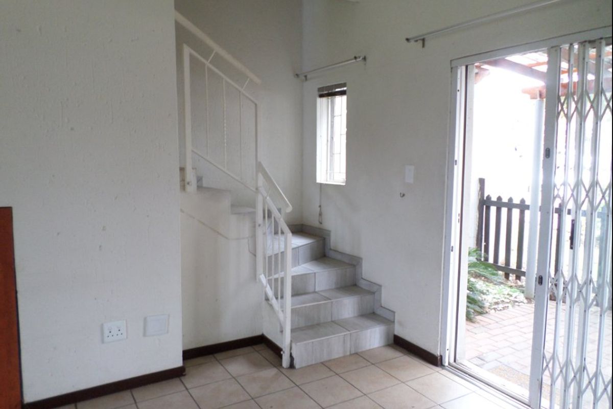 An empty living area featuring tiled flooring, a staircase with a metal balustrade, and a sliding glass door providing access to an outdoor space.