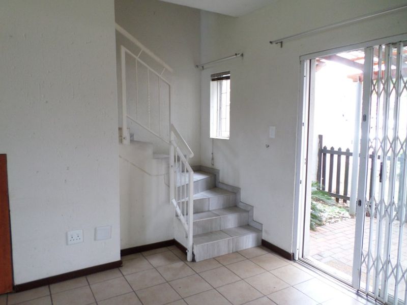 An empty living area featuring tiled flooring, a staircase with a metal balustrade, and a sliding glass door providing access to an outdoor space.