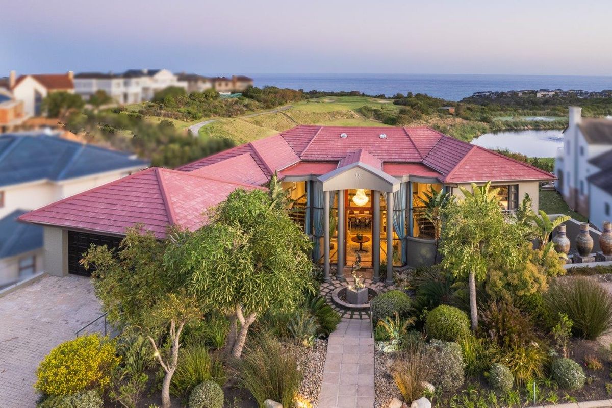 Aerial view of a well-maintained residential property featuring a tiled roof, double garage, landscaped garden, and a prominent covered entrance portico.