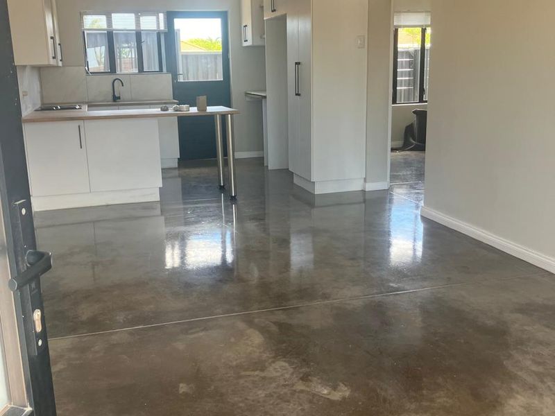 Open plan kitchen and living area featuring polished concrete floors, modern white cabinetry, and a breakfast bar, offering a clean and contemporary living space.