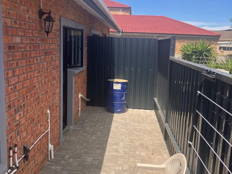 A paved rear exterior area featuring a brick facade, metal privacy screening, and external plumbing fixtures, suitable for a utility or service space.