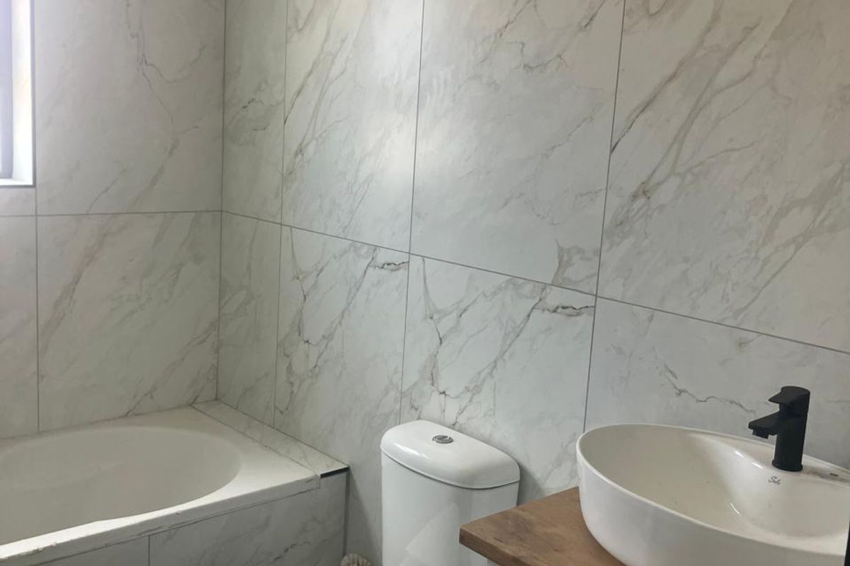 Modern bathroom featuring marble-look wall tiles, a built-in bathtub, a contemporary vanity with a vessel sink, and a toilet.