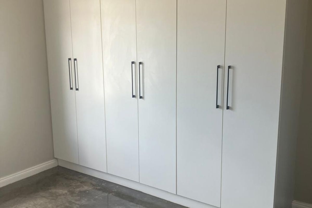 A clean, minimalist bedroom featuring a large white built-in wardrobe and polished concrete flooring.