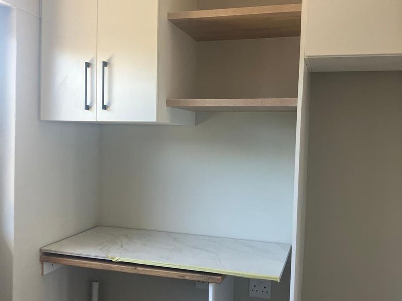 A functional scullery or utility area featuring built-in white cabinetry, open shelving, and a marble-look countertop, currently awaiting final finishing touches.