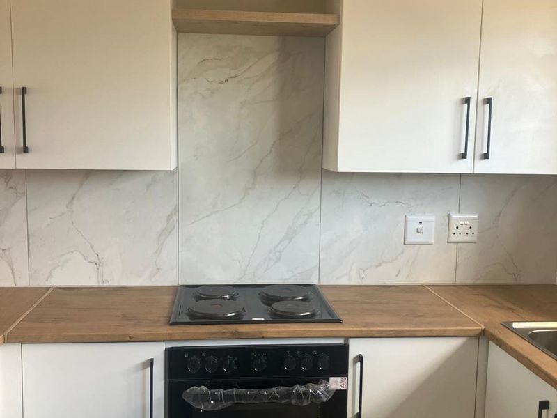 Modern kitchen featuring white cabinetry, wooden countertops, a marble-look splashback, and a built-in oven with an electric hob.