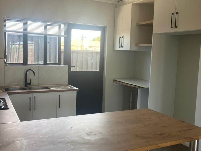 A clean, modern kitchen featuring white cabinetry, wooden countertops, a double sink, and a built-in hob, with direct access to the rear exterior.