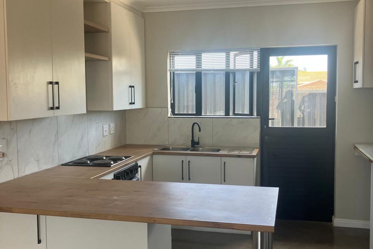 A modern, clean kitchen featuring white cabinetry, wooden countertops, a built-in hob, and a double sink with direct access to the exterior.